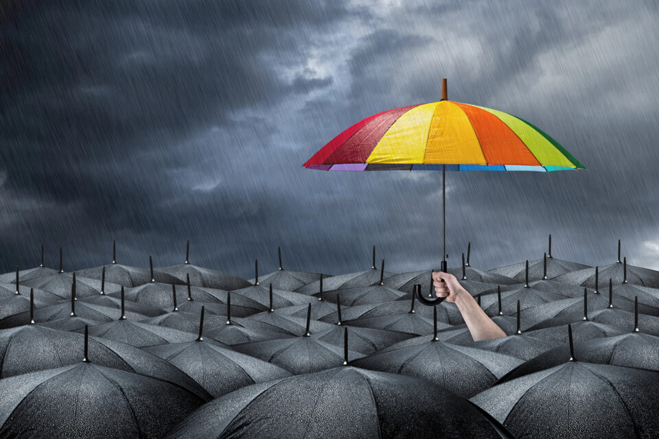 a hand holding up a brightly colored umbrella above the other black umbrellas during a storm